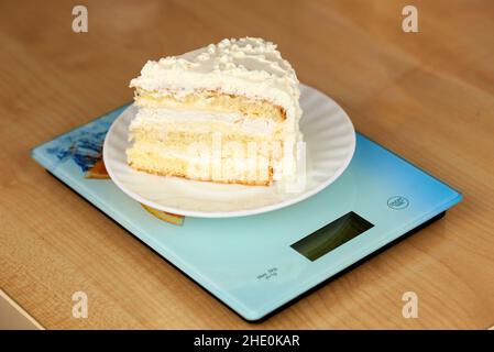 Un pedazo de delicioso pastel con crema de mantequilla blanca yace en las escamas. Concepto de conteo de calorías, seguimiento de figuras Foto de stock
