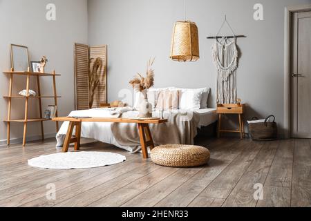 Dormitorio elegante con banco de madera cerca de una cómoda cama Foto de stock