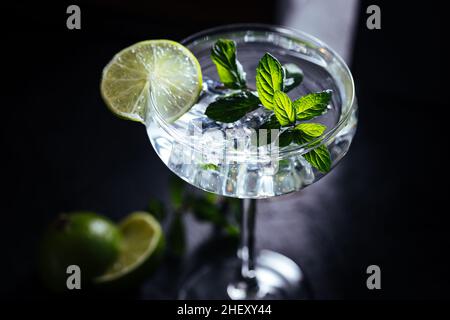 Tónico Gin en cóctel de vidrio con hielo, hojas de menta y cal en un oscuro tablero rústico