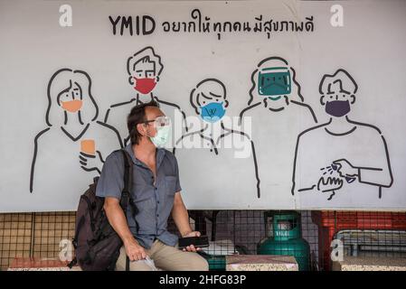 Bangkok, Tailandia. 16th de Ene de 2022. Un hombre que lleva máscara facial como medida preventiva contra la propagación del covid-19 está cerca de una pancarta publicitaria en el Monumento a la Victoria en Bangkok. Crédito: SOPA Images Limited/Alamy Live News Foto de stock