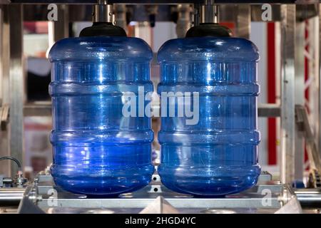 Depósito de almacenamiento de agua de PE azul o botella de PEA en la línea de producción de la cinta transportadora en la máquina de llenado de bebidas en la fabricación de agua potable. Foto de stock