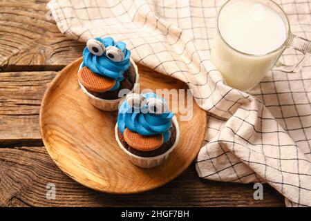 Plato con sabrosos y divertidos cupcakes y un vaso de leche para la celebración de Halloween sobre fondo de madera Foto de stock