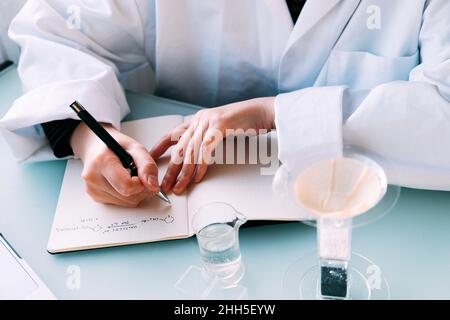 Un joven científico que escribe la fórmula química en el libro en el laboratorio Foto de stock