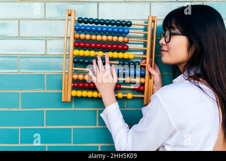 Mujer joven contando cuentas en abaco por pared de ladrillo Foto de stock