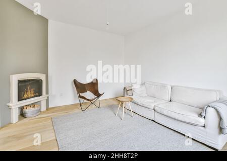 Auténtica foto de un cómodo interior de sala de estar con chimenea, una  mesa redonda sobre alfombra gris, una elegante silla y un sofá blanco  Fotografía de stock - Alamy