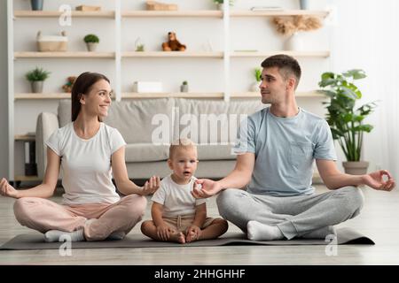 Yoga en casa. Feliz Familia Joven con el Bebé Pequeño Meditando Juntos Foto de stock