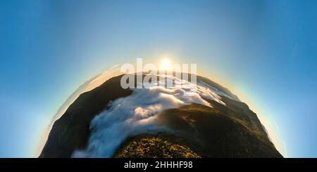 Vista aérea desde la altitud elevada del pequeño planeta tierra al amanecer cubierto de bosques perennes y altos picos montañosos. Foto de stock