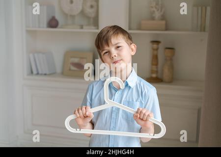 pequeño niño caucásico sostiene el colgador habitación contra la pared de fondo con