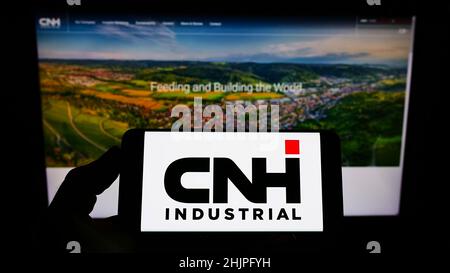 Persona que sostiene un smartphone con el logotipo de la empresa de equipos pesados CNH Industrial N.V. en la pantalla delante del sitio web. Enfoque en la pantalla del teléfono.
