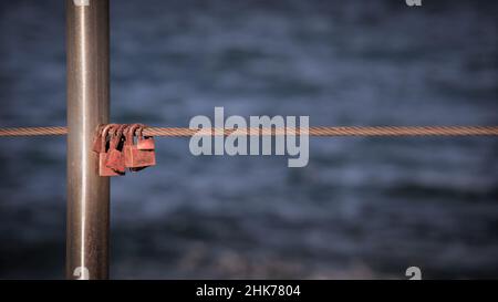 Candados Colgantes sobre cable metálico Rusty contra el mar Foto de stock