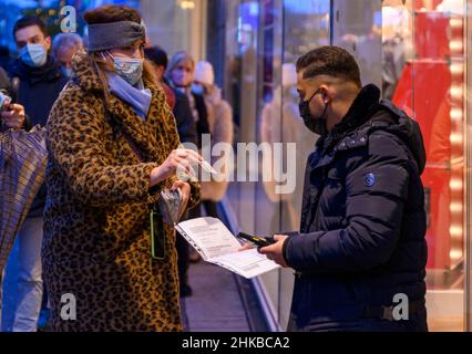 Los pasaportes de vacunación se comprueban en la entrada de una boutique de moda en el centro de la ciudad de Düsseldorf, NRW, Alemania, en 11.12.2021 Foto de stock