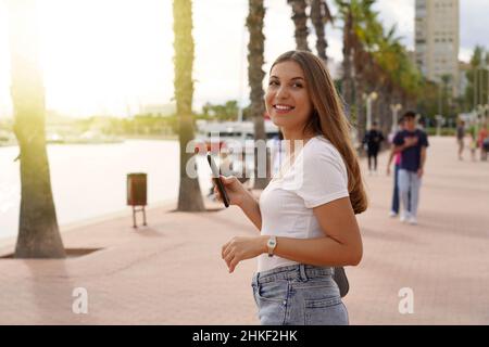 Adolescente usando su celular en la orilla del agua mientras pasea al atardecer Foto de stock