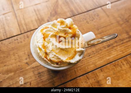 Frappe (frappuccino) de café frío, con crema batida y jarabe de caramelo, con cuchara sobre una mesa de madera