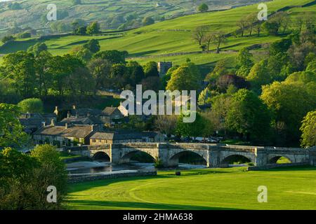 Pintoresco Burnsall soleado en el valle (puente de 5 arcos, atractivas casas de campo, torre de la iglesia, verdes campos de ladera) - Yorkshire Dales, Inglaterra, Reino Unido. Foto de stock