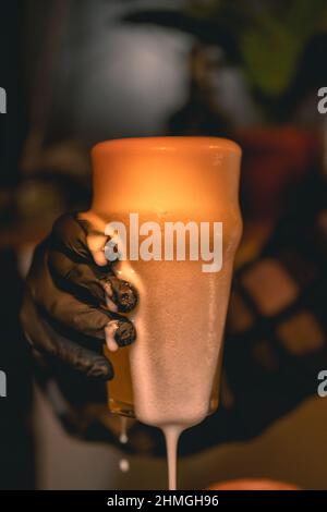 Barman mano sosteniendo un vaso de cerveza fresca espumosa ligera Foto de stock