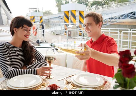 Alegre joven vertiendo buen vino en vaso para su novia cuando están disfrutando de un fin de semana romántico en yate