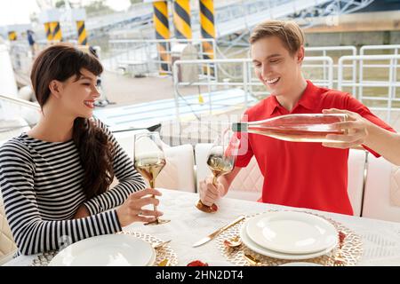 Feliz pareja joven bebiendo buen vino cuando disfruta de una cena romántica en barco