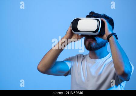 Primer plano retrato de un joven guapo hombre barbudo en gafas vr jugando videojuegos con auriculares de realidad virtual en un metaverse.