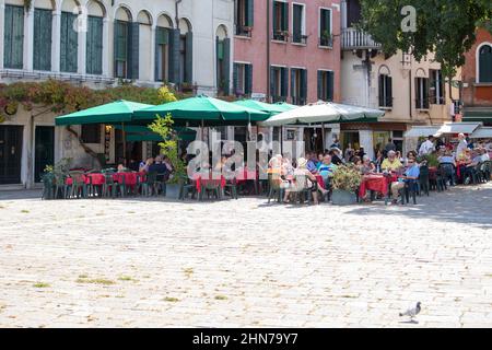 turistas en uno de los muchos cafés y restaurantes situados en las calles venecianas Foto de stock