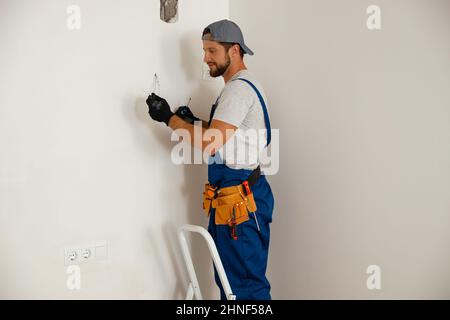 Electricista de mano ocupado sosteniendo un destornillador mientras trabaja en un sistema eléctrico residencial Foto de stock