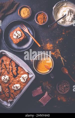 Brownies caseros con taza de café y ingredientes para hornear sobre fondo marrón Foto de stock