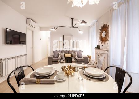 Mesa de comedor redonda blanca con servicio de comida al lado de una tv y sala de estar con suelo de madera Foto de stock