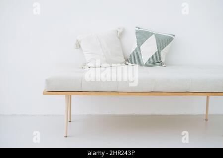 Banco de madera minimalista con almohadas de lino de estilo ecológico sobre fondo de pared blanco Foto de stock