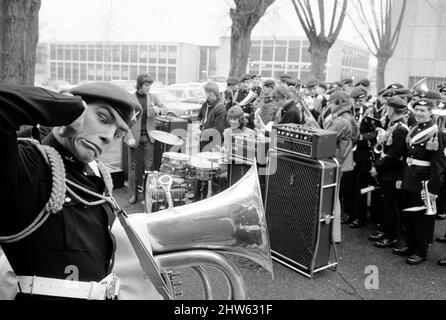 Dave Dee, Dozy, Beaky, Mick y Tich tocan números mientras que la banda regimental del Batallón 1st del Regimiento de Parachute cubre los oídos de los thgeir en el cuartel de Montgomery Lines, Aldershot. La banda está apareciendo en el espectáculo 'Contrast' con el grupo pop en el Albert Hall el 1968 de noviembre