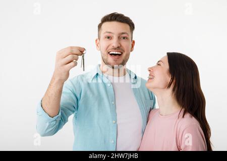 Una joven y alegre pareja se abraza en la cocina, sosteniendo las llaves de una nueva casa en sus manos. Felices recién casados se mudaron a un apartamento nuevo, conseguí un Foto de stock