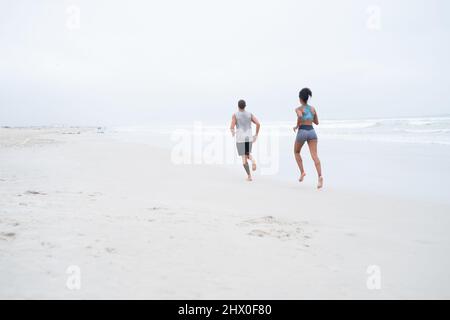 Preparar sus cuerpos de playa para el verano. Foto de vista trasera de una joven pareja corriendo juntos por la playa. Foto de stock