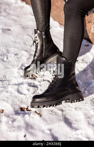 Mujer con botas negras de moda sobre nieve blanca de cerca piernas de mujer  con elegantes botas de cuero de invierno