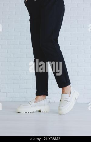 Patas de una joven hermosa mujer en pantalones negros y modernos mocasines  de cuero blanco. Nueva colección de zapatos para mujer primavera-verano 2022  Fotografía de stock - Alamy