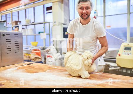 Joven como aprendiz de panadero amasa masa en preparación para hornear pan en la panadería Foto de stock