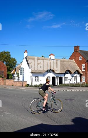 Bonita casa de campo tradicional de paja encalada inglesa en el centro del pueblo con un ciclista en primer plano, Kings Bromley, Staffordshire, Inglaterra, Foto de stock