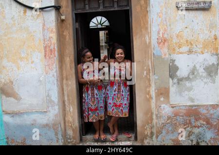 Dos mujeres cubanas jóvenes vestidas igual se ríen en la puerta de su hogar en La Habana, Cuba. Foto de stock