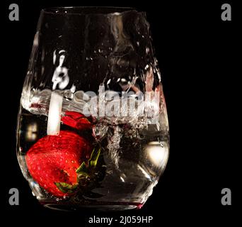 Fresa roja madura en un vaso con agua y salpicaduras sobre un fondo negro con espacio de copia.
