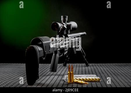 Moderno potente rifle de francotirador con una mirilla telescópica montada sobre un bipod. Munición y un almacén adicional junto al rifle. Foto de stock
