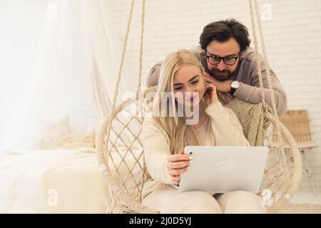 una linda pareja caucásica sentada en un inddor canta mientras ve una película o algo más en un ordenador portátil. Fotografías de alta calidad Foto de stock