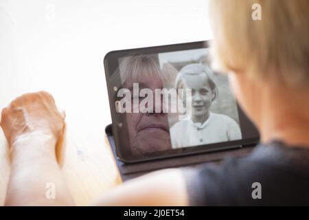 Senior mujer caucásica mirando fotos viejas de ella, como una mujer joven en un equipo tablet pc
