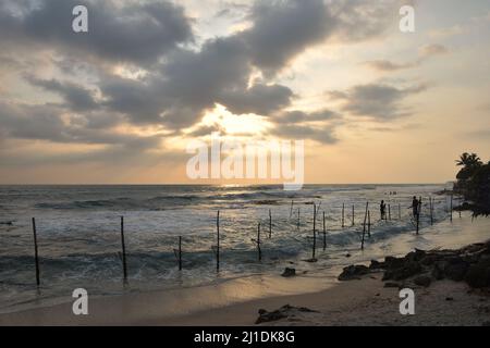 Puesta de sol sobre la costa sur de Sri Lanka, con pescadores en zancos en la distancia Foto de stock