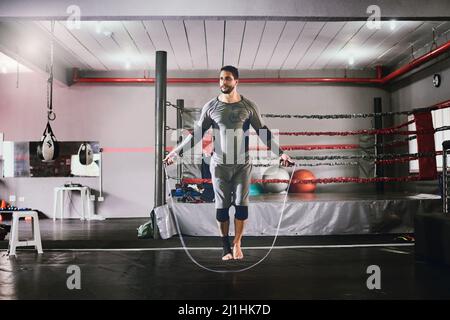 Esto es lo que hago antes de cada sesión. Tiro de un boxeador masculino joven enfocado usando una cuerda de salto para ejercicios de entrenamiento dentro de un gimnasio durante el día Foto de stock
