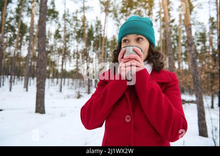 Bonita mujer europea de pelo oscuro con un abrigo de lana de invierno rojo  brillante y un sombrero de punto verde bebiendo té o café de una taza  térmica, descansando en un Fotografía de stock - Alamy