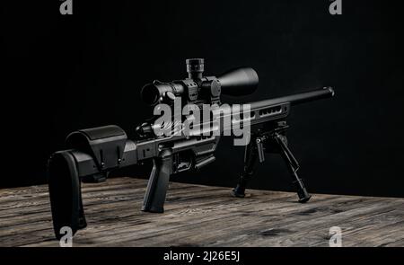 Moderno y potente rifle de francotirador con una vista telescópica montada en un bipod. Fondo oscuro. Foto de stock