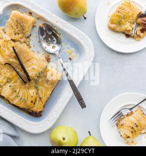 Una tarta de pera al revés con porciones en platos a un lado. Foto de stock