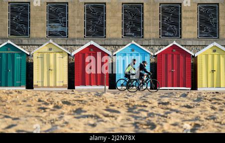 La gente pasa en bicicleta por cabañas de playa en la playa de Boscombe en Dorset. Fecha de la foto: Domingo 3 de abril de 2022.
