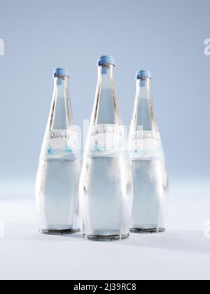 3D Representación de tres botellas de vidrio de agua espumosa con etiqueta falsa sobre fondo azul Foto de stock