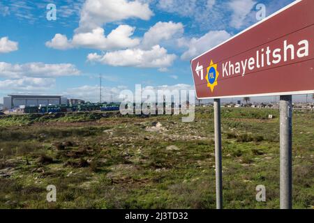 Sudáfrica, Ciudad del Cabo, señal de la autopista del municipio de Khayelitsha. Casas Nuevas y Centro Comunitario a la izquierda, casas antiguas a la distancia a la derecha. Foto de stock