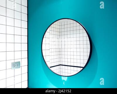 Azulejos blancos de cerámica con diseño de rejilla vista a la pared del baño reflejada en una forma redonda grande del espejo sobre fondo de pared azul, estilo mínimo.