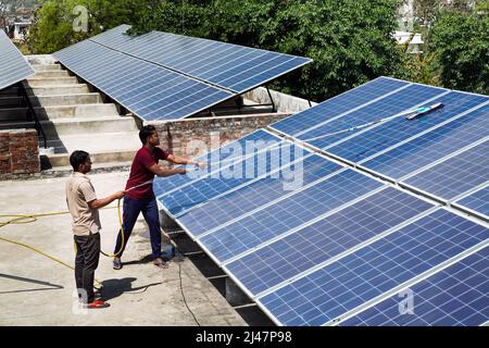 Hombres limpiando paneles solares en el techo del Instituto de Filosofía y Religión Vishwa Jyoti Gurukul de la Sociedad Misionera India IMS en Varanasi, Uttar Pradesh, India Foto de stock