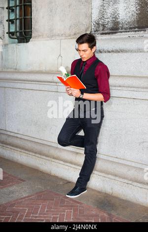Vestirse en una camisa roja, un chaleco jeans negros y una corbata negra, un joven guapo está leyendo un libro rojo con una rosa Fotografía de - Alamy